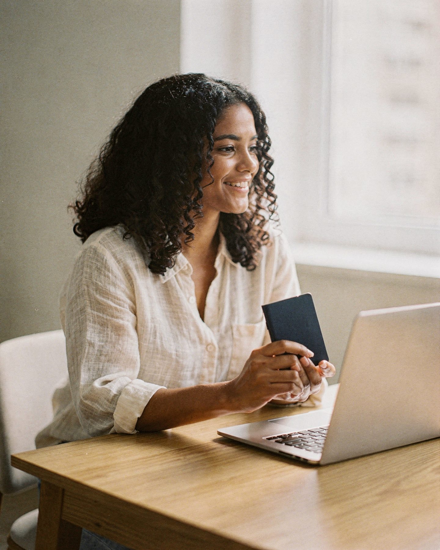 Uma mulher sorrindo com um passaporte na mão diante de um notebook